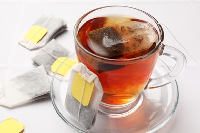 Photo of Tea bags and cup of aromatic drink on white table, closeup