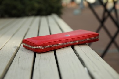 Red purse on wooden bench outdoors, closeup. Lost and found