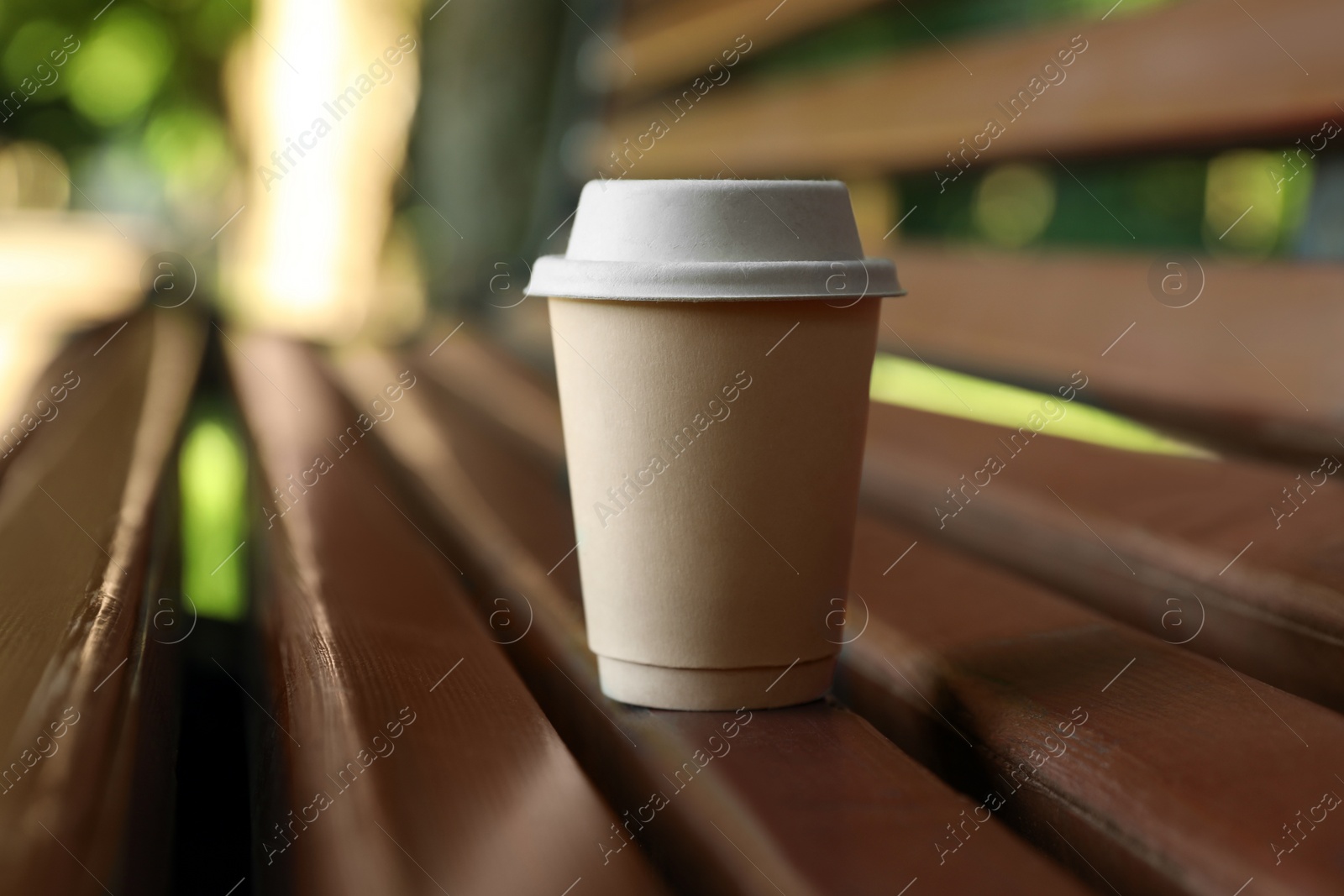 Photo of Cardboard takeaway coffee cup with lid on wooden bench outdoors, space for text