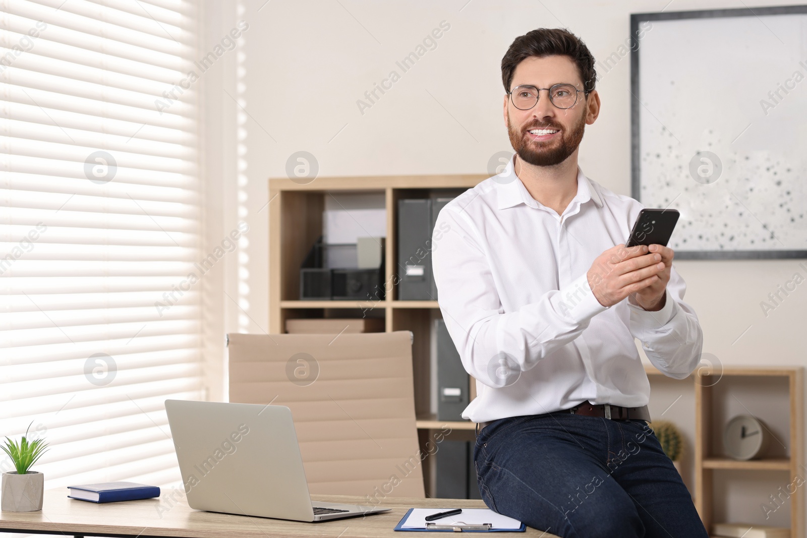 Photo of Smiling man with smartphone in office. Space for text