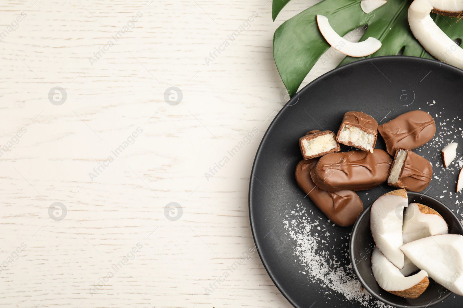 Photo of Delicious milk chocolate candy bars with coconut filling on white wooden table, flat lay. Space for text