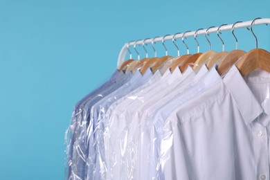 Photo of Dry-cleaning service. Many different clothes in plastic bags hanging on rack against light blue background, closeup and space for text