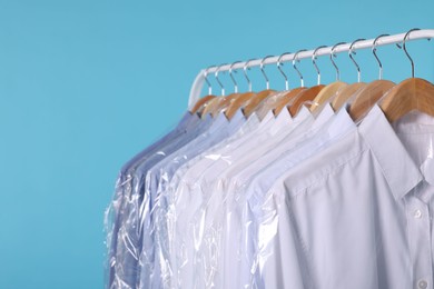 Dry-cleaning service. Many different clothes in plastic bags hanging on rack against light blue background, closeup and space for text