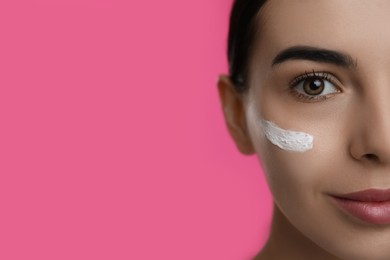 Photo of Young woman with cream on face against pink background, closeup. Space for text