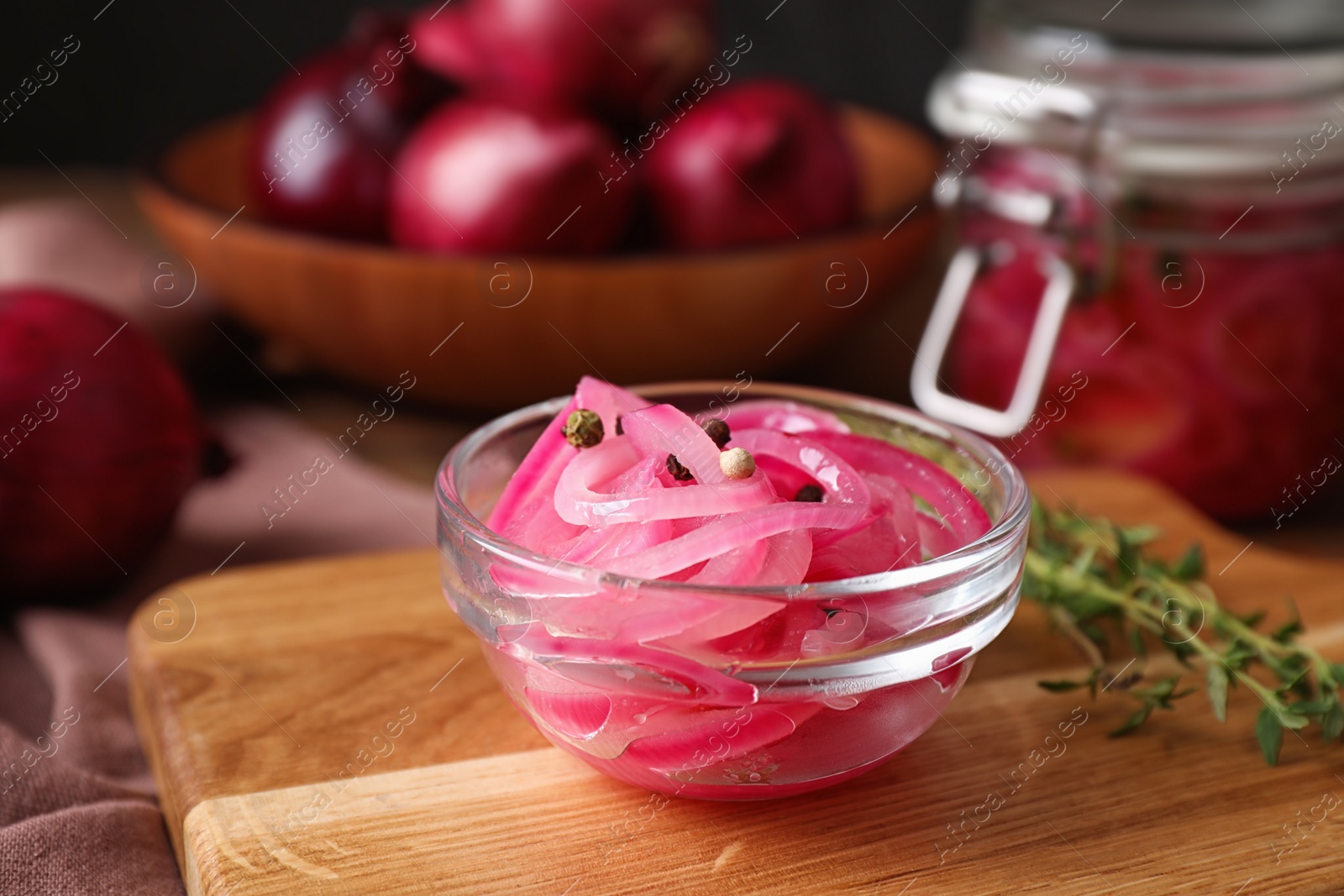 Photo of Bowl with tasty pickled onions on wooden cutting board