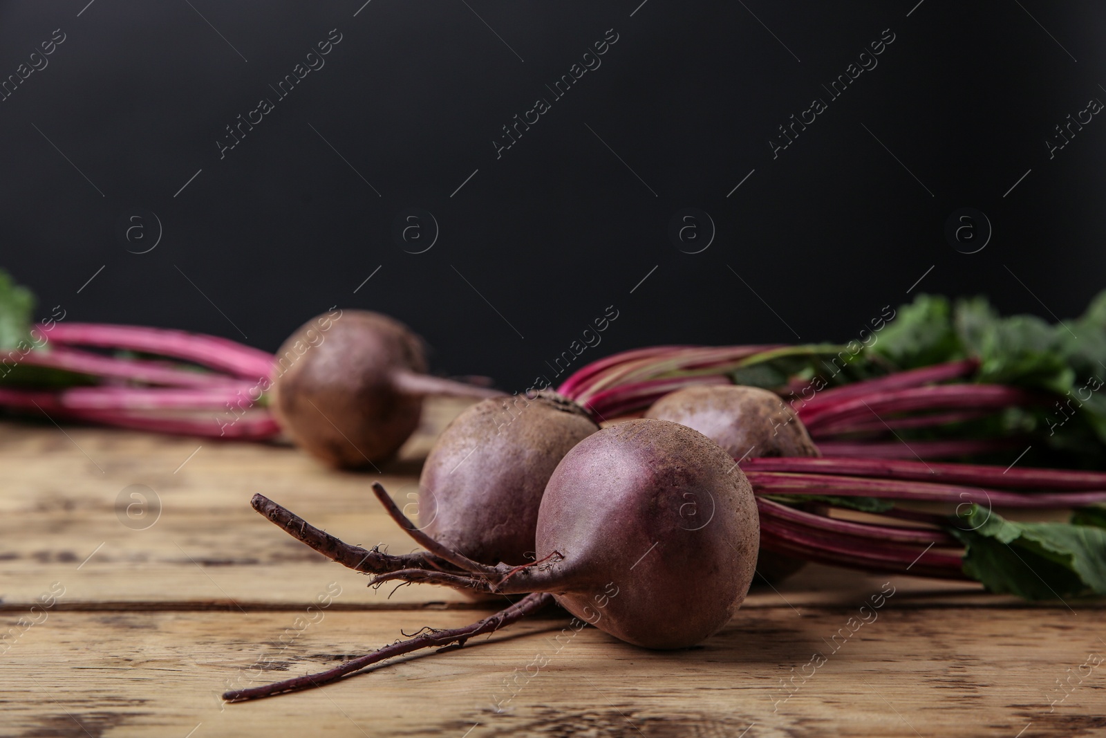 Photo of Fresh beets with leaves on wooden table against black background. Space for text