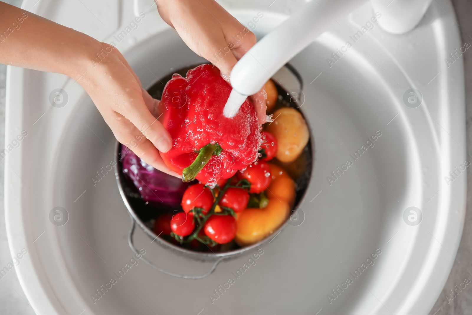 Photo of Woman washing fresh vegetables in kitchen sink, top view