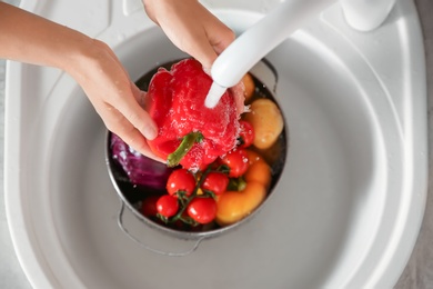 Photo of Woman washing fresh vegetables in kitchen sink, top view