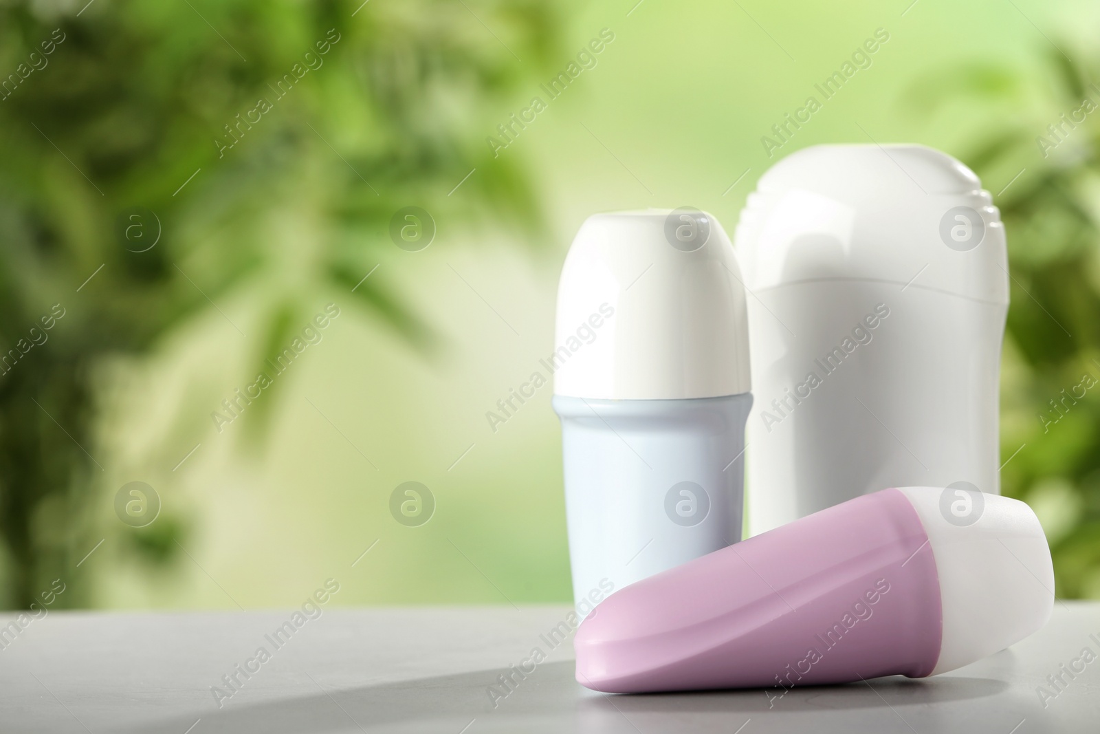 Photo of Different deodorants on white wooden table against blurred background. Space for text