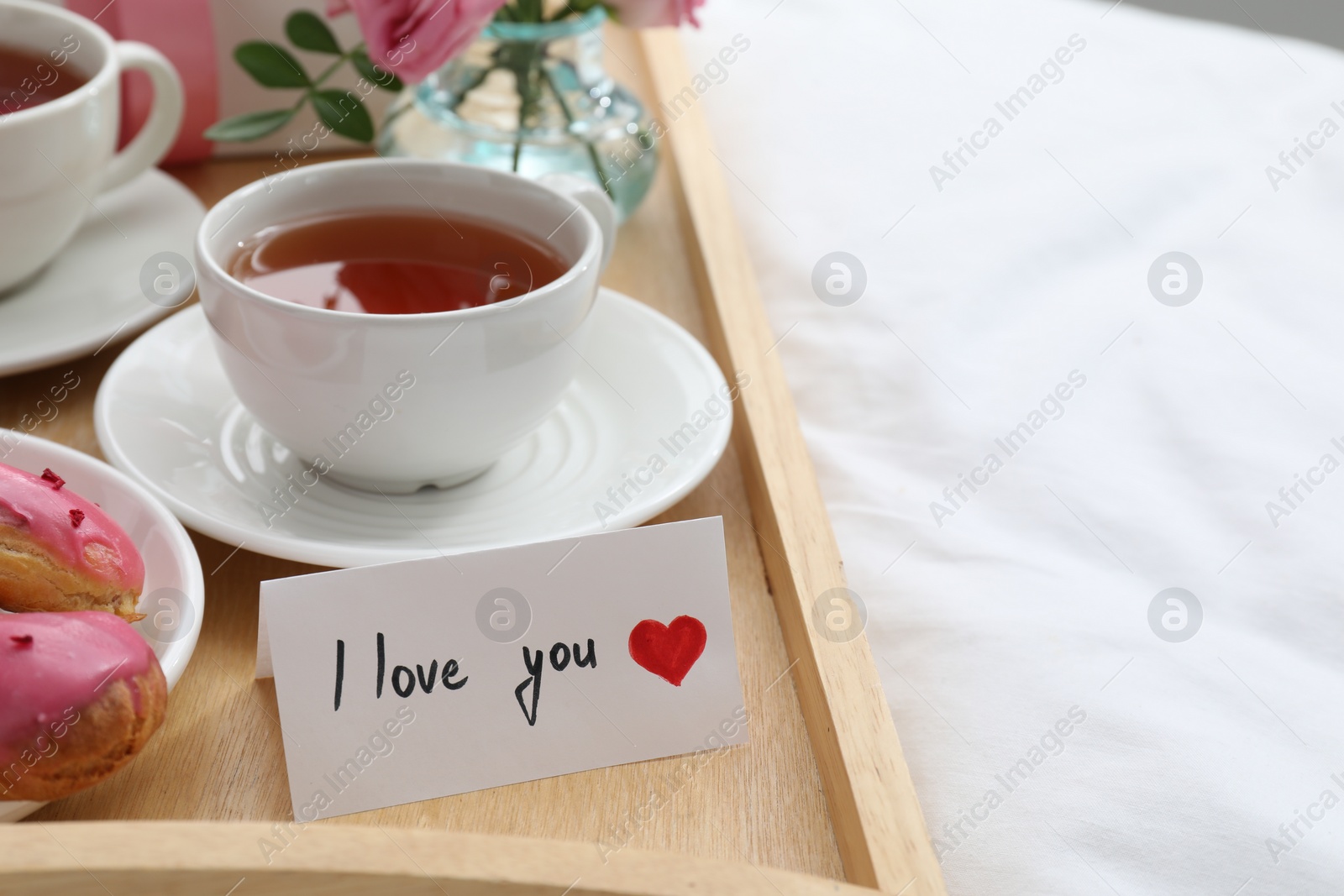 Photo of Tasty breakfast served in bed. Delicious eclairs, tea and card with phrase I Love You on tray, closeup. Space for text