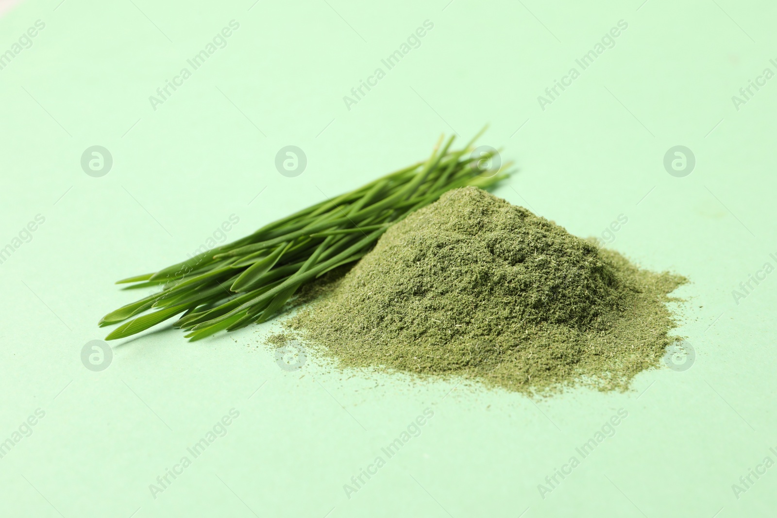 Photo of Pile of wheat grass powder and fresh sprouts on green table, closeup