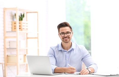 Photo of Handsome young man working with laptop at table in office