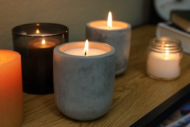 Lit candles in different holders on wooden table indoors