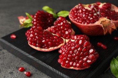 Photo of Cut fresh pomegranate and green leaves on grey table, closeup
