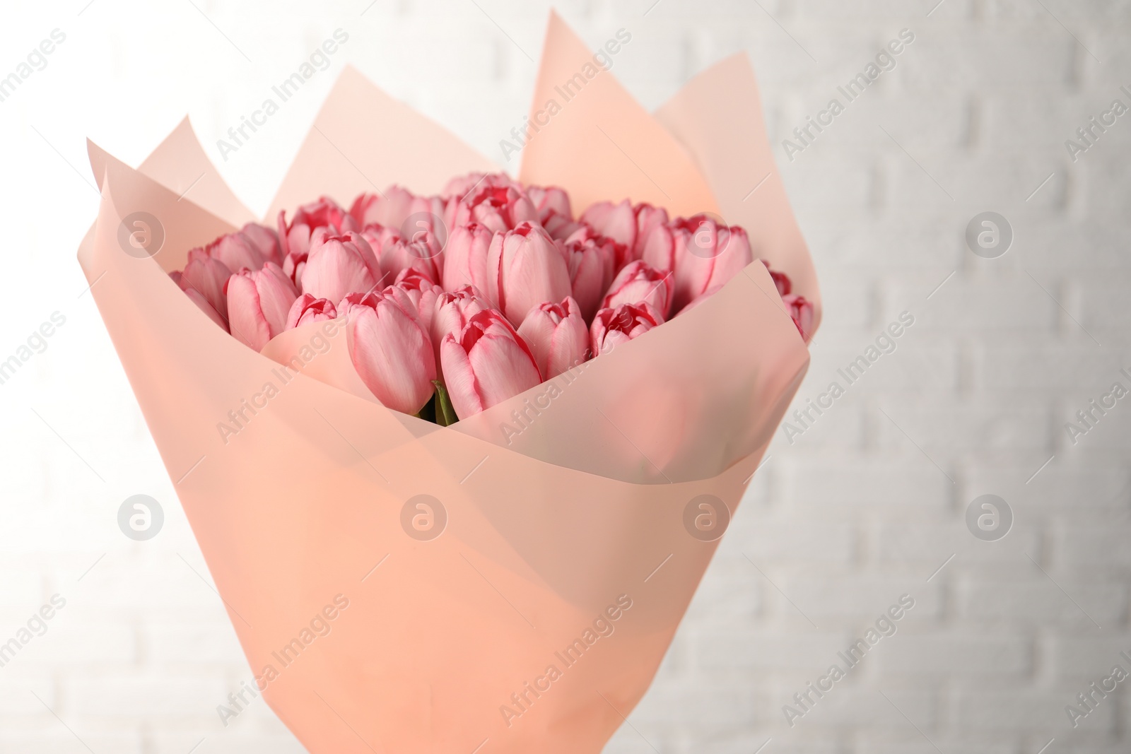 Photo of Bouquet of beautiful pink tulips near white brick wall, closeup. Space for text