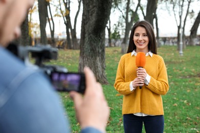Young journalist and video operator working in park