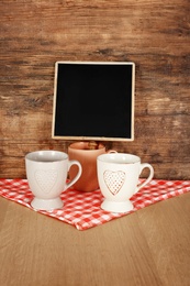 Photo of Ceramic cups on table near small chalkboard