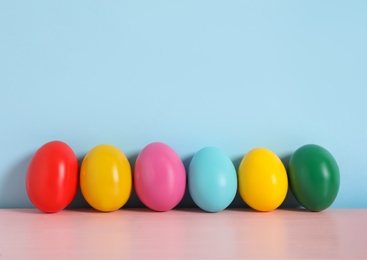 Photo of Easter eggs on pink wooden table against light blue background, space for text