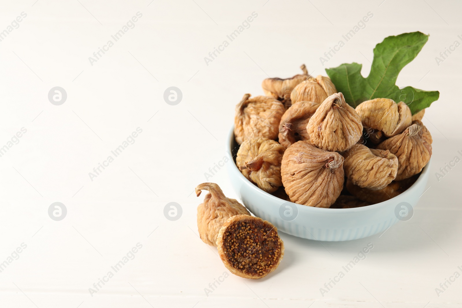 Photo of Bowl with tasty dried figs and green leaf on white wooden table. Space for text