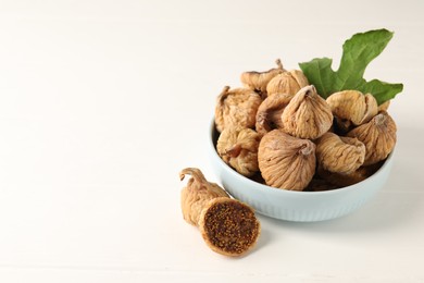 Bowl with tasty dried figs and green leaf on white wooden table. Space for text