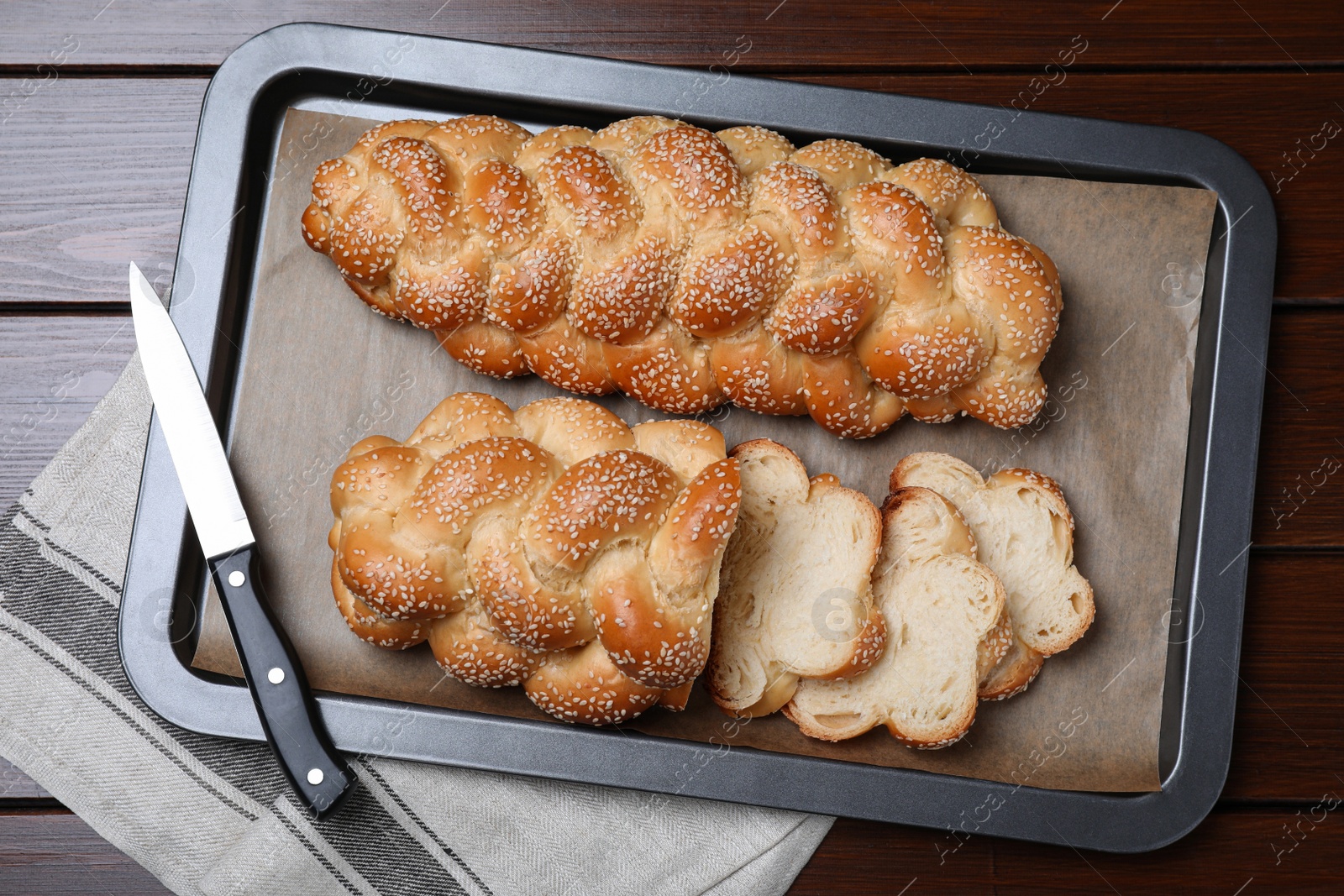 Photo of Baking tray with homemade braided bread and knife on wooden table, top view. Traditional Shabbat challah