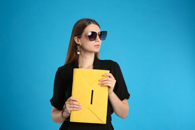 Photo of Beautiful young woman with stylish yellow bag on light blue background
