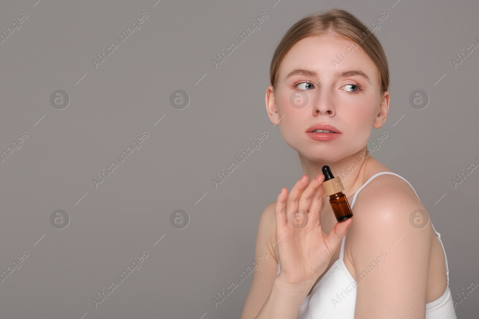 Photo of Beautiful young woman with essential oil on light grey background. Space for text