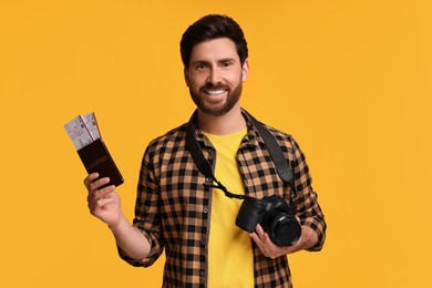Smiling man with passport, tickets and camera on yellow background