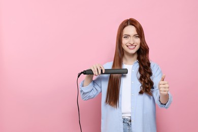 Photo of Beautiful woman with hair iron showing thumbs up on pink background, space for text