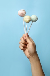 Woman holding sweet cake pops on light blue background, closeup