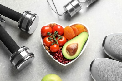 Photo of Heart shaped bowl with healthy products and sports equipment on grey background, flat lay