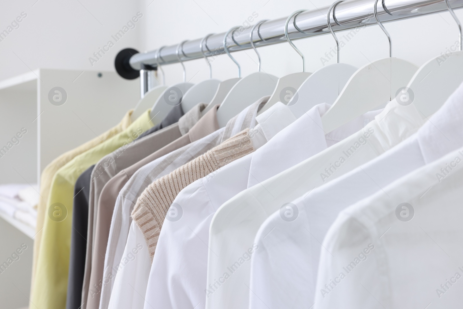 Photo of Rack with different stylish shirts near white wall, closeup. Organizing clothes