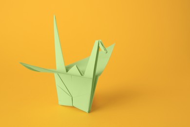 Origami art. Beautiful light green paper crane on orange background, space for text