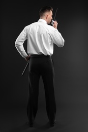 Male security guard using portable radio transmitter on dark background