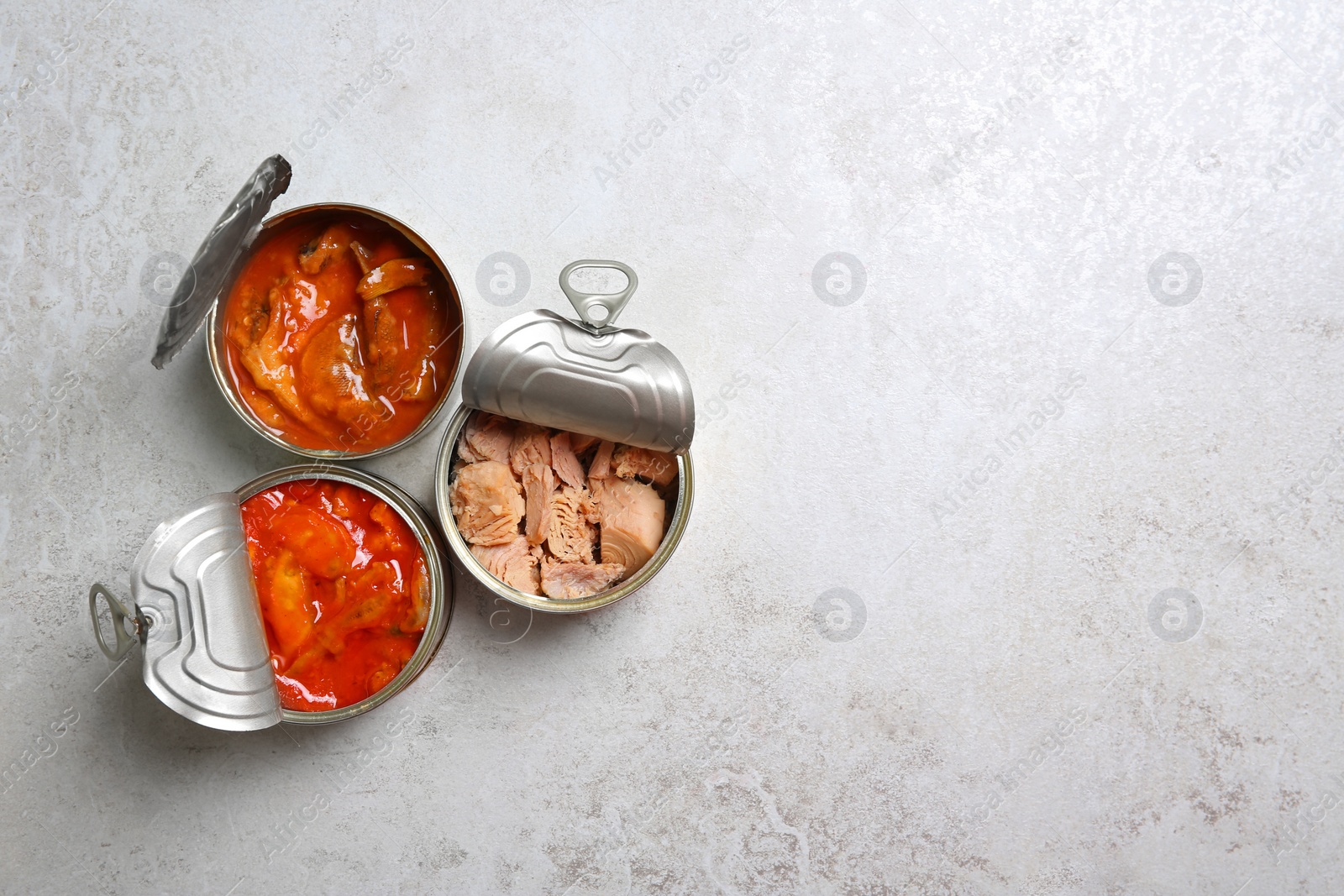 Photo of Tin cans with fish on grey table, flat lay. Space for text