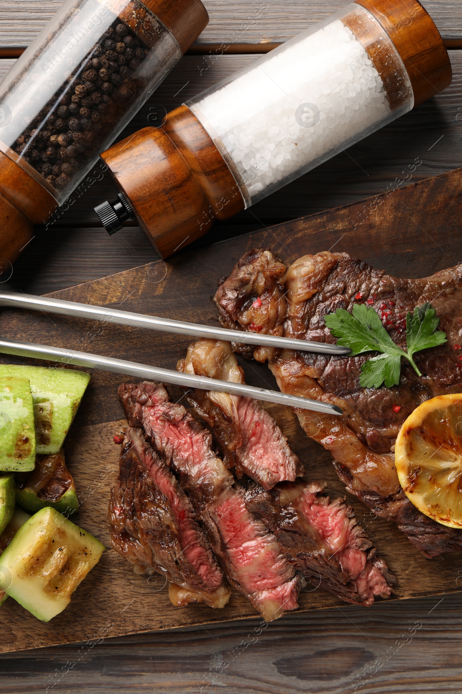 Photo of Delicious grilled beef steak and vegetables served on wooden table, top view