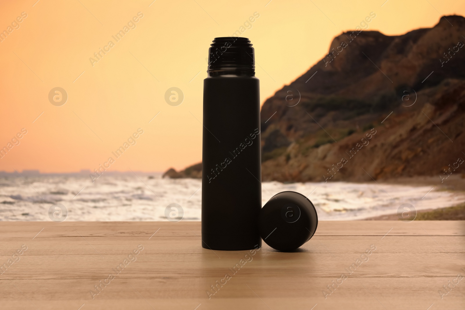 Image of Thermos on wooden table near sea at sunset