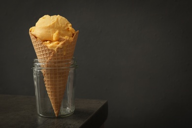 Delicious yellow ice cream in wafer cone and glass jar on grey table. Space for text