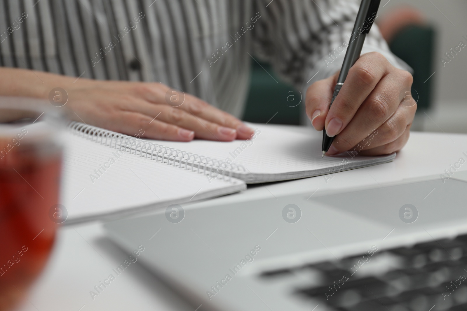 Photo of Left-handed woman writing in notebook at table indoors, closeup