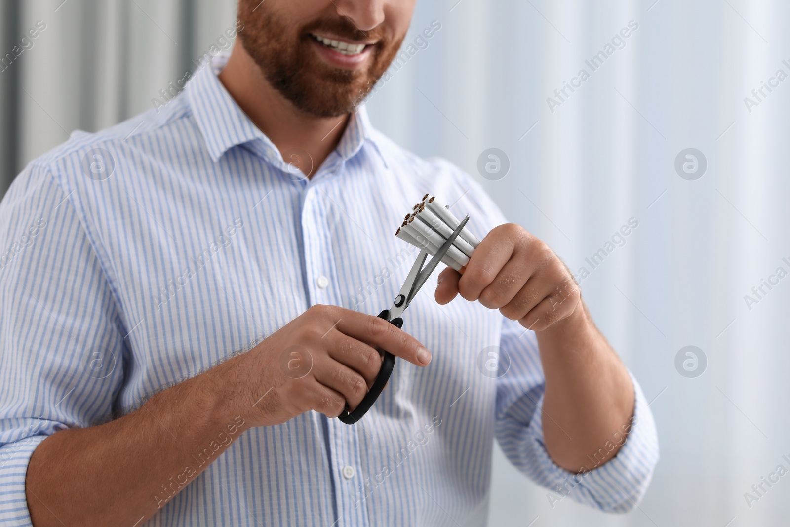 Photo of Stop smoking concept. Man cutting cigarettes on light background, closeup