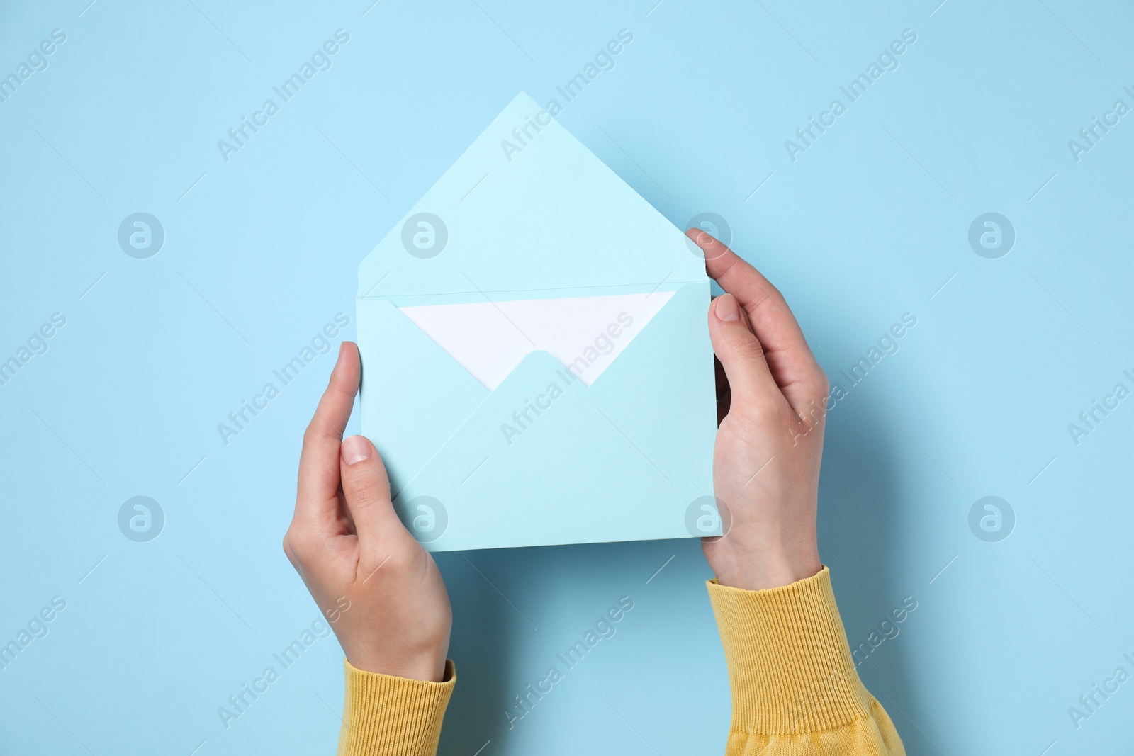 Photo of Woman holding letter envelope with card at light blue table, top view