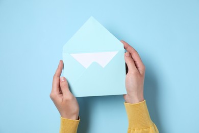 Woman holding letter envelope with card at light blue table, top view