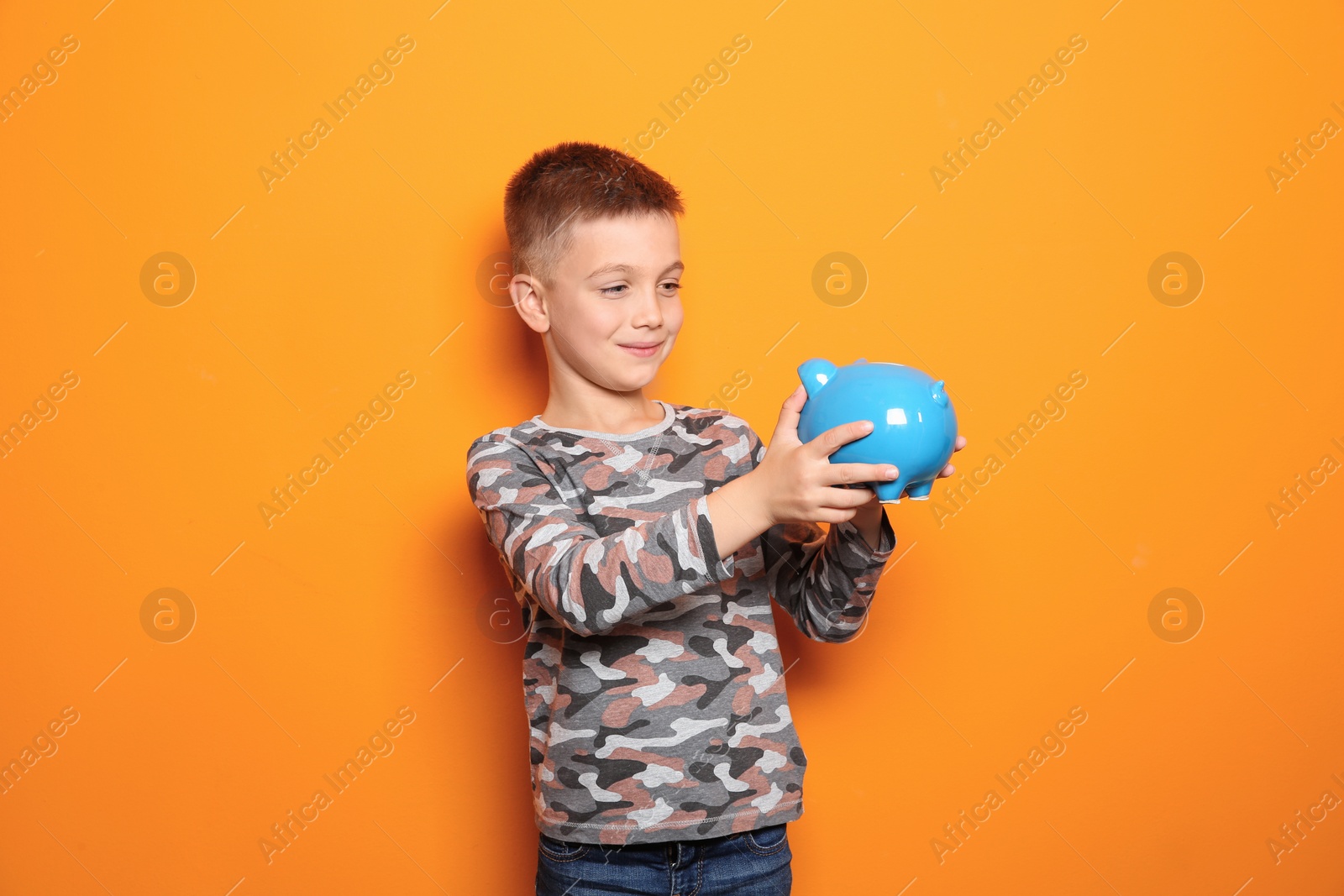 Photo of Little boy with piggy bank on color background