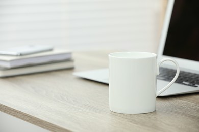 White ceramic mug and laptop on wooden table indoors. Space for text