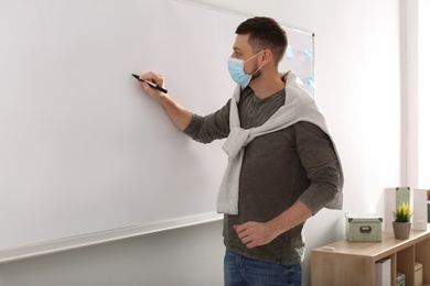 Teacher with protective mask writing on board in classroom. Reopening after Covid-19 quarantine