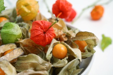 Photo of Ripe physalis fruits with dry husk and colorful sepals on white table, closeup