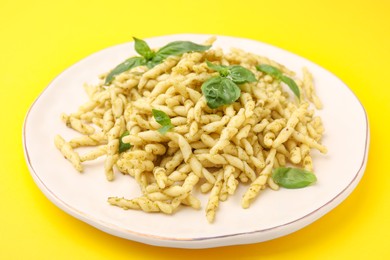 Photo of Plate of delicious trofie pasta with pesto sauce and basil leaves on yellow background