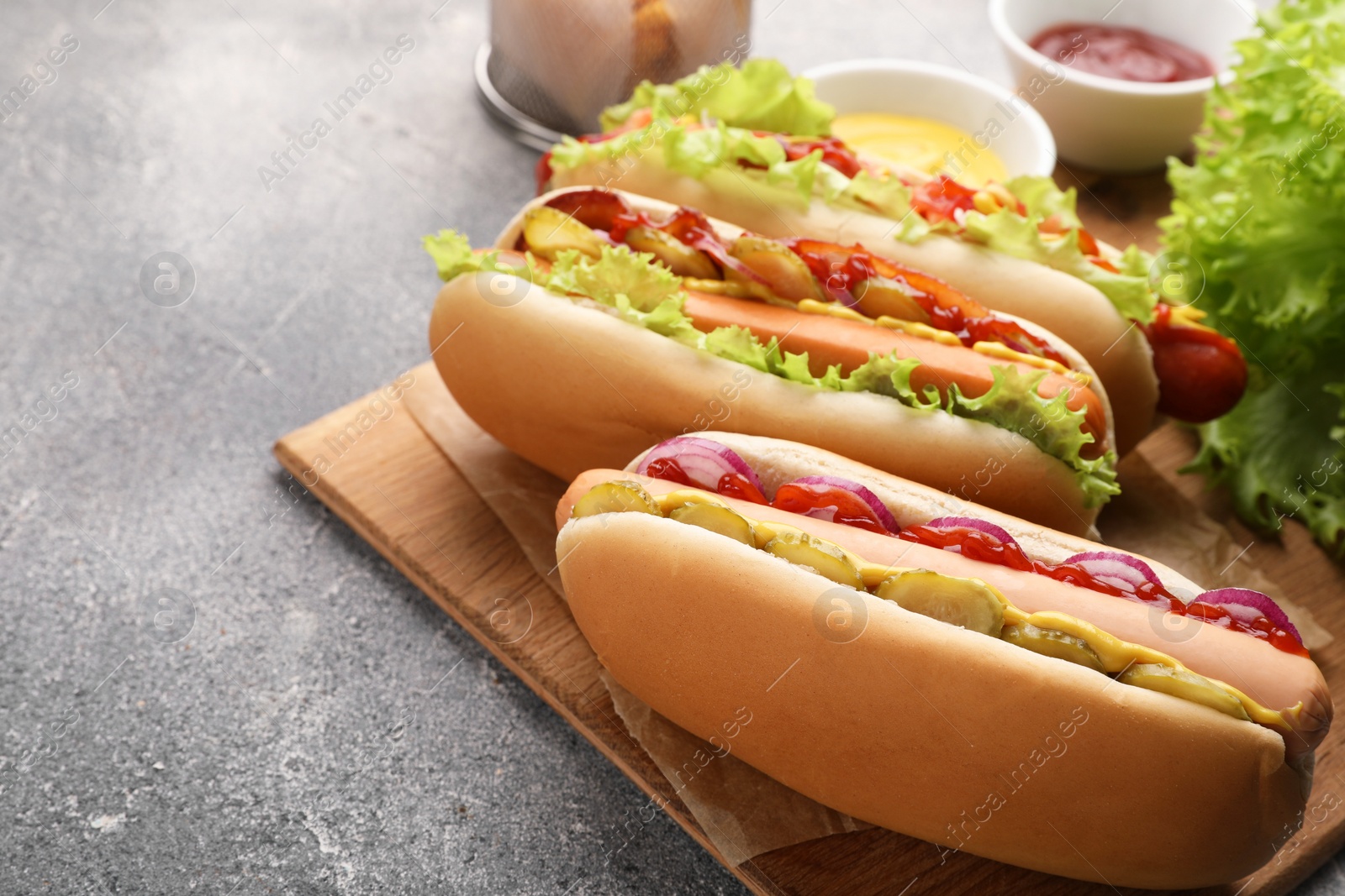 Photo of Delicious hot dogs with different toppings served on grey table. Space for text