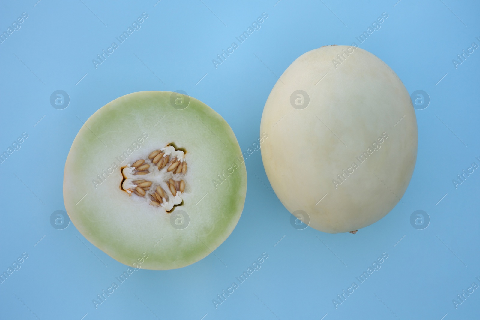 Photo of Whole and cut fresh ripe honeydew melons on light blue background, flat lay