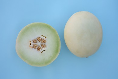 Whole and cut fresh ripe honeydew melons on light blue background, flat lay